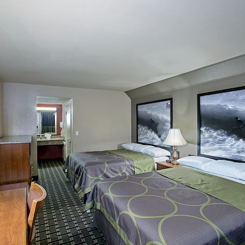 The image shows a hotel room with two double beds, a desk, a wall-mounted TV, and a bathroom in the background. Ending the sentence.