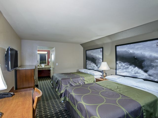 A wide-angle view of a hotel room with two beds, a desk, and a bathroom in the background.