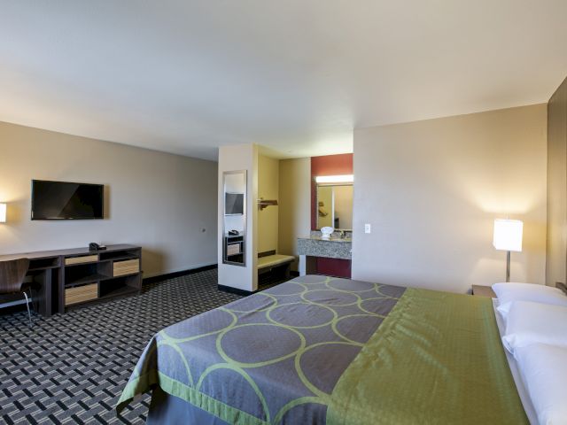 A wide view of a hotel room with a bed, desk, TV, and bathroom in the background.