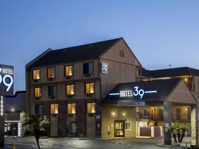 A three-story hotel building with a lit sign reading 'Hotel 39' and a parking lot in front.
