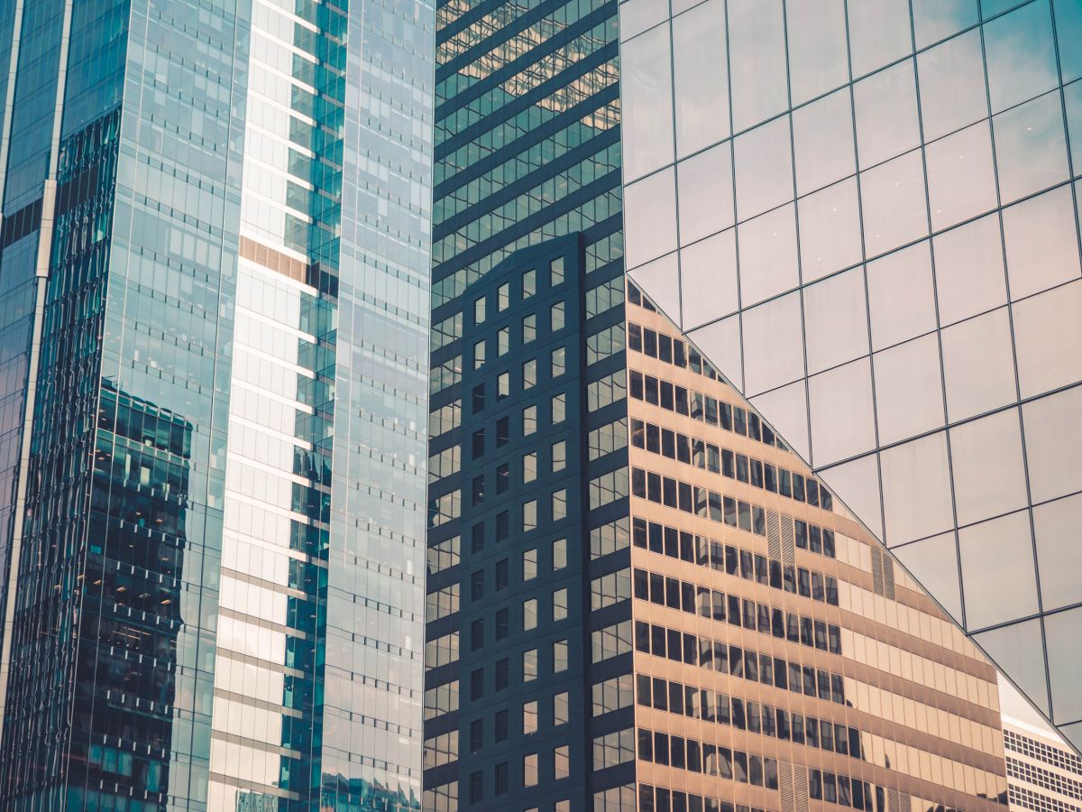 The image shows several modern skyscrapers with glass windows reflecting buildings and the sky, creating a pattern of lights and shadows.