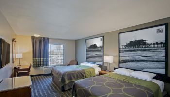 A hotel room with two double beds, a window, a desk, a TV, and large black-and-white beach photos above the beds.