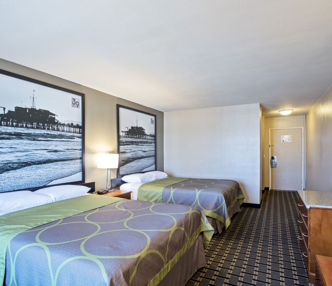 A hotel room with two beds, nightstand, lamp, and large art on the walls.