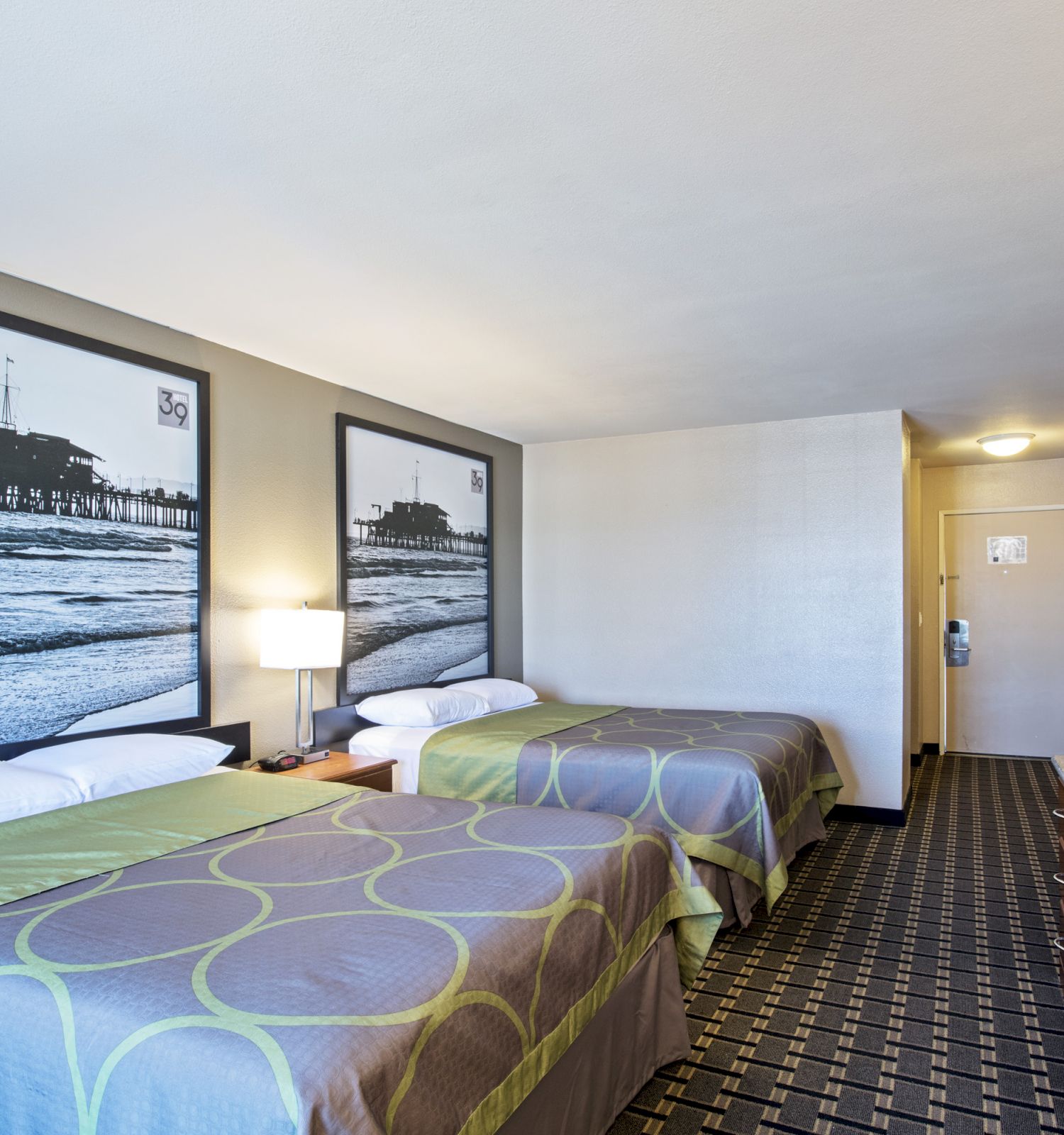 A hotel room with two beds, wall art, a television, and a door to the hallway.